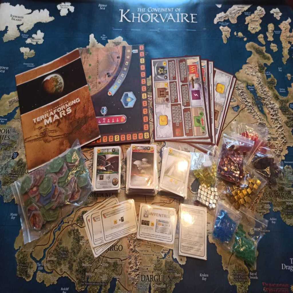 The contents of the Terraforming Mars base box. Moving clockwise, from the top left: Rules, Game Board, Player Boards, Player and Resource cubes, Reference cards, Corporations, Tiles, and in the middle the Project cards.