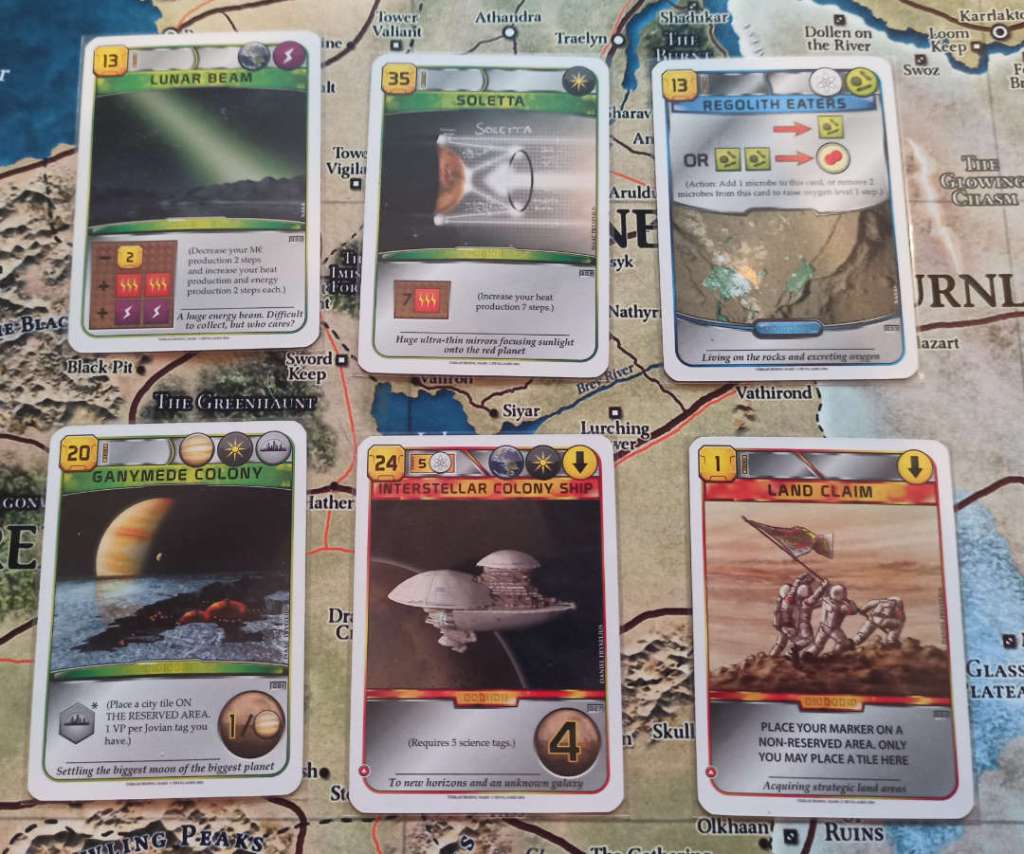Moving clockwise starting from the far left, the cards are: Lunar Beam, costing 13 credits with an Earth and Energy tag - reduce credit production by 2, increase energy and heat production by 2. Soletta, costing 35 credits with a space tag: increase heat production by 7. Regolith Eaters, costing 13 credits with a Science and Microbe tag: As an action, add a Microbe resource, or remove 2 Microbes to increase Oxygen by 1. Land Claim, an event costing 1 credit: Place a marker on a non-reserved area of the map, only you may place a tile there. Interstellar Colony Ship, an even costing 24 credits with an Earth and Space tag: requires 5 Science tags and gives 4 VP. Ganymede Colony, costing 20 credits with a Jovian, Space, and City tag: Place a city tile on the reserved area, you gain 1 VP per Jovian tag you have.
