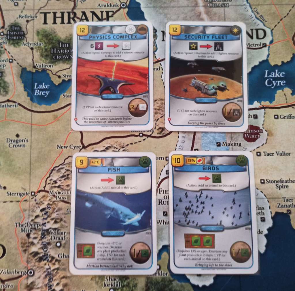 The 4 cards pictures each have an action and are, moving clockwise from the top left: 
Physics Complex, for 6 energy adds a science resource on it- each science resource gives 2 VP. Security Fleet, for 1 titanium adds a Fighter resource - each fighter gives 1 VP. Fish, action adds 1 animal resource - each animal gives 1 VP. Birds, action adds 1 animal resource - each animal gives 1 VP.